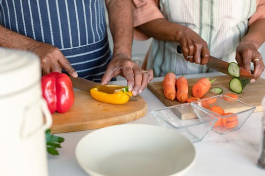 Midsection of arfican american senior couple cutting vegetables and preparing meal together. healthy retirement lifestyle at home.