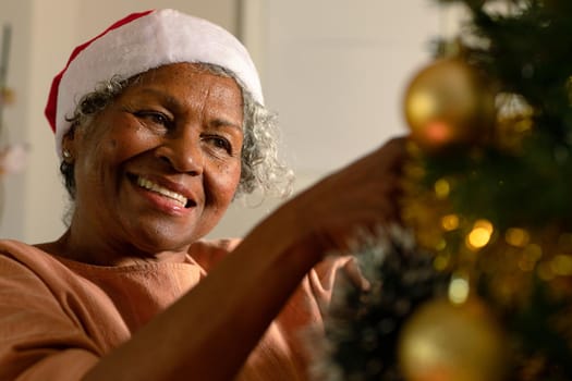 Happy african american senior woman decorating christmas tree. christmas, festivity and tradition at home. festivity together at home.