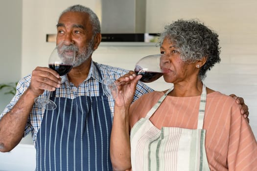 Happy arfican american senior couple drinking wine together in kitchen. healthy retirement lifestyle at home.
