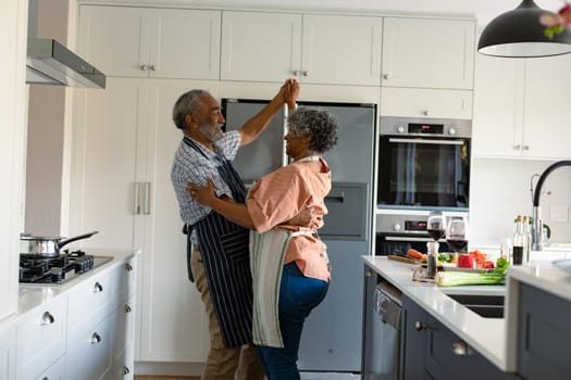 Happy arfican american senior couple dancing together in kitchen and having fun. healthy retirement lifestyle at home.