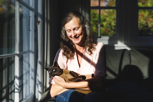 Happy senior caucasian woman in bedroom, holding her pet cat. retirement lifestyle, spending time alone at home.