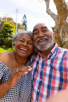 Happy african american senior couple taking selfie and hugging. active retirement lifestyle at home and garden.