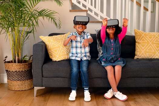 Happy african american sibling sittings on sofa, holding vr headset and having fun. childhood, leisure and discovery using technology at home.