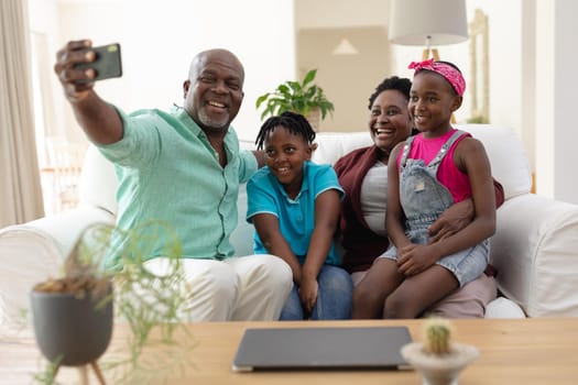 African american grandfather and grandmother on couch smiling with grandchildren taking selfie. happy family spending time together at home.
