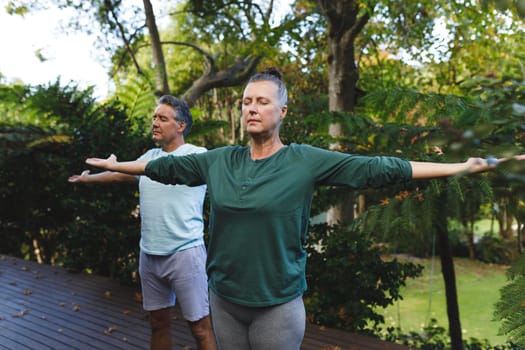 Happy senior caucasian couple practicing yoga, stretching in sunny garden. healthy retirement lifestyle, spending time at home.