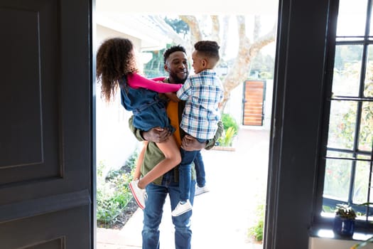 Happy african american children welcoming their father coming back home. family time, having fun together at home.