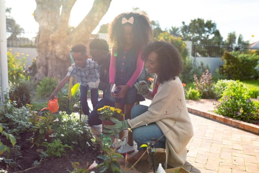 Happy african american family planting flowers and watering plants together. family time, having fun together at home and garden.