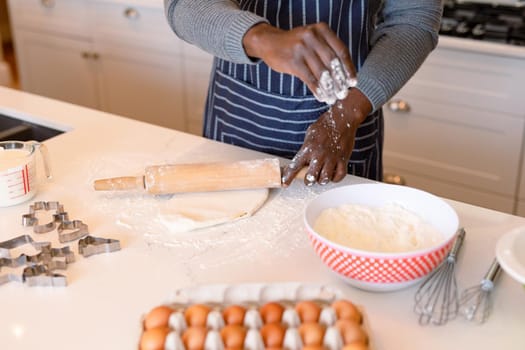 Midsection of african american man wearing apron, baking in kitchen. cooking and baking, spending time at home.