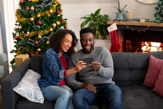 Happy african american couple having video call on smartphone, christmas decorations in background. christmas, festivity and communication technology.