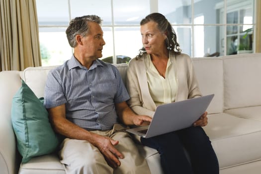 Happy senior caucasian couple in living room, sitting on sofa, using laptop. retirement lifestyle, spending time at home.