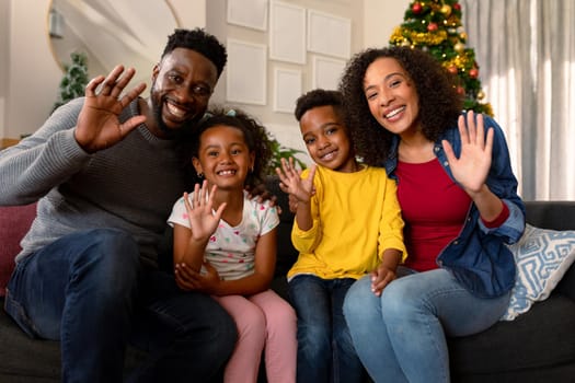 Happy african american family waving, having video call, christmas decorations in background. christmas, festivity and communication technology.