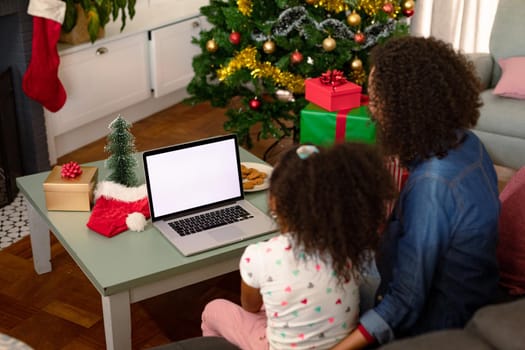 Back view of african american mother and daughter using laptop with copy space on screen. christmas, festivity and communication technology.