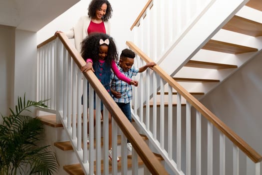 Happy african american mother and children walking downstairs. family time, having fun together at home.