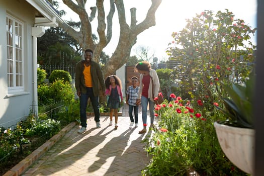 Happy african american family holding hands and walking outside. family time, having fun together at home and garden.