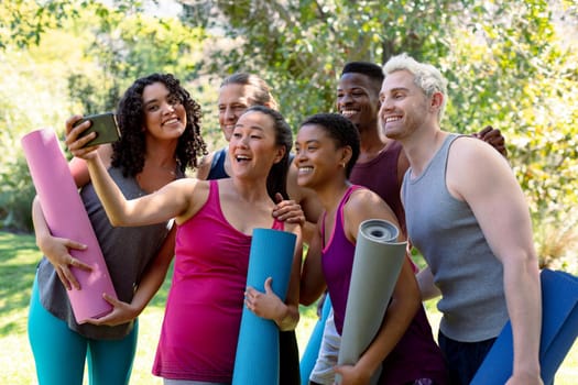 Group of happy fit diverse female and male friends holding yoga mats and taking selfie. fitness and healthy, active lifestyle.