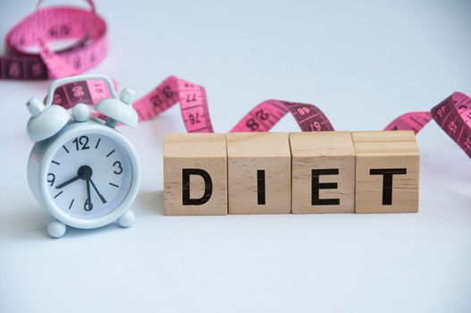 Diet text on wooden blocks with alarm clock and measuring tape background. Weight loss and fitness concept