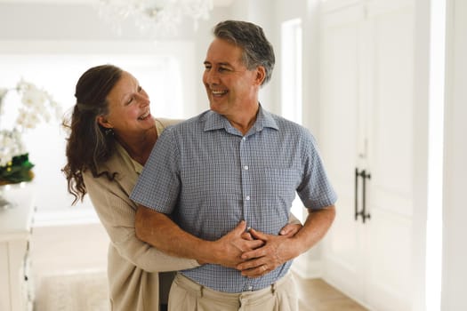 Happy senior caucasian couple in living room, embracing and smiling. retirement lifestyle, spending time at home.