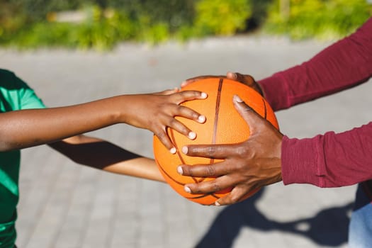 Midsection of african american father and son holding basketball together in garden. family spending time at home.