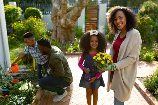 Happy african american mother and daughter looking at camera, gardening with family. family time, having fun together at home and garden.