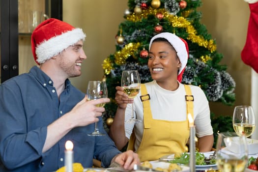 Happy diverse female and male friends in santa hats toasting, celebrating christmas with friendse. christmas festivities, celebrating at home with friends.