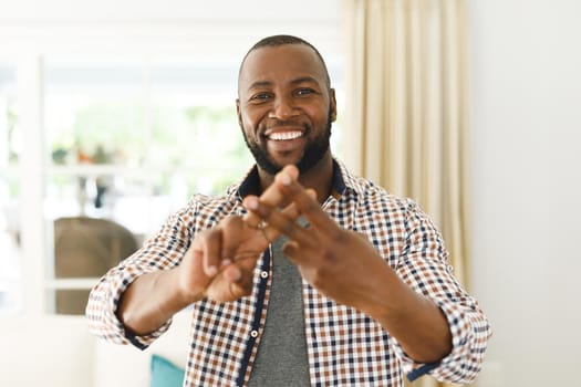 Portrait of african american man smiling and looking at camera in living room talking sign language. communication without words.