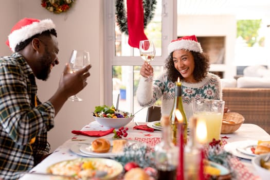 Happy african american couple making toast at christmas table. family christmas time and festivity together at home.