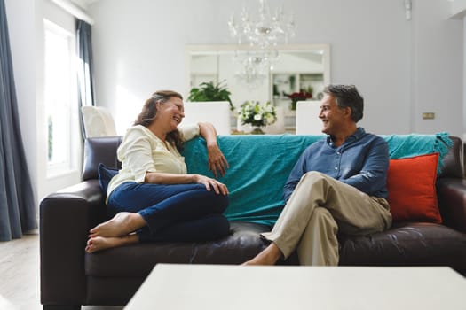 Happy senior caucasian couple in living room sitting on sofa, talking. retirement lifestyle, spending time at home.