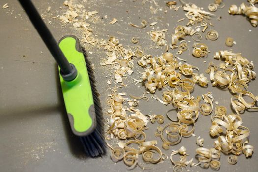a small pile of wood shavings on a gray linoleum floor with plastic broom brush