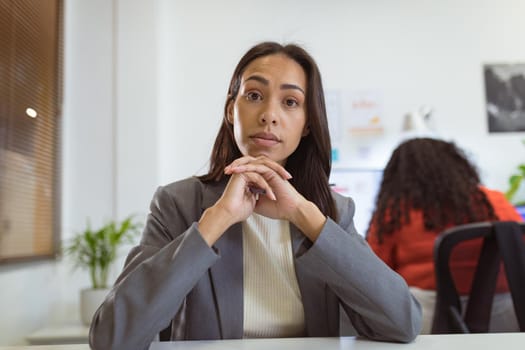 Thoughtful biracial businesswoman sitting at desk making video call in modern office. business and office workplace.