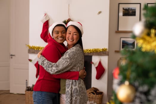 Two happy diverse female friends in santa hats taking photo at christmas time. christmas, festivity and communication technology.