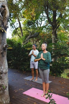 Happy senior caucasian couple practicing yoga, meditating in sunny garden. healthy retirement lifestyle, spending time at home.