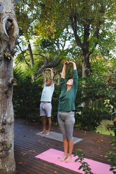 Happy senior caucasian couple practicing yoga, stretching in sunny garden. healthy retirement lifestyle, spending time at home.