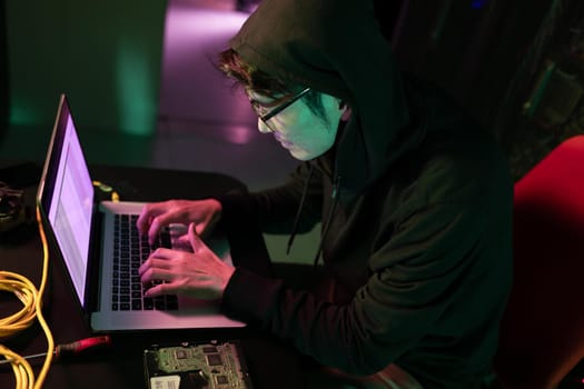 Asian male hacker using a laptop in computer server room. cyber crime and hacking concept