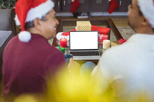 Happy biracial adult son and senior father in santa hats making laptop christmas video call. christmas, festivity and communication technology.