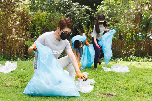 Asian parents, son and daughter in face masks putting rubbish in refuse sacks in the countryside. eco conservation volunteers, countryside clean-up during covid pandemic.