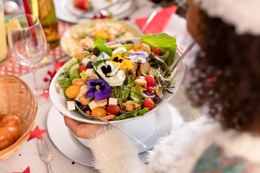 Hand of african american woman holding bowl with salad. christmas, festivity and tradition at home.