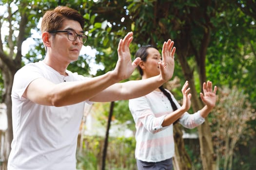 Asian couple wearing white shirts exercising outdoors, practicing tai chi. family fitness time in garden.