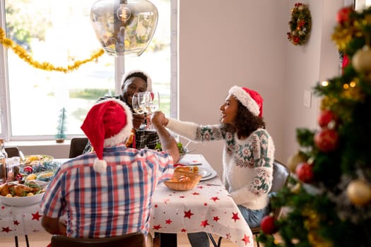 Happy multi generation family wearing santa hats, toasting with vine, having christmas meal. family christmas time and festivity together at home.