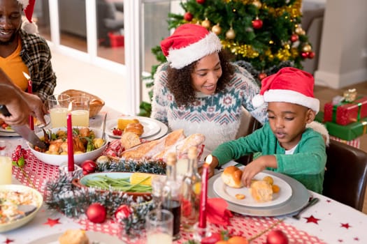 Happy african american mother and son wearing santa hats at christmas table. family christmas time and festivity together at home.