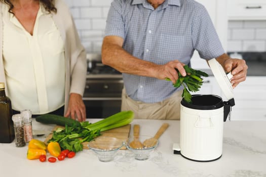 Midsection senior caucasian couple in modern kitchen, cooking together composting organic waste. retirement lifestyle, spending time at home.