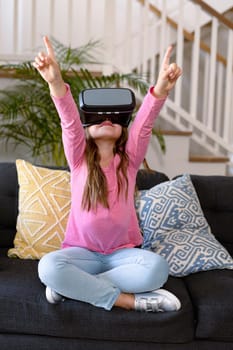 Happy caucasian girl sitting on sofa, wearing vr headset, having fun. childhood, leisure and discovery using technology at home.