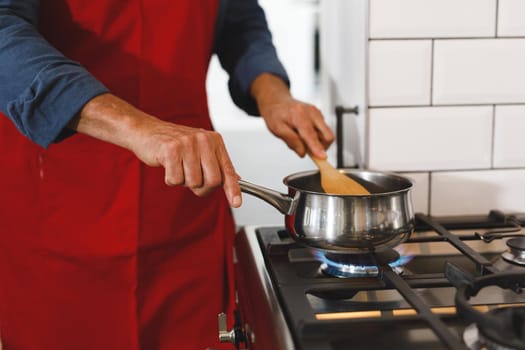 Midsection of senior caucasian man wearing apron in kitchen cooking. retirement lifestyle, spending time at home.