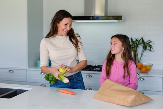 Happy caucasian mother and daughter unpacking groceries in kitchen. family time, having fun together at home.