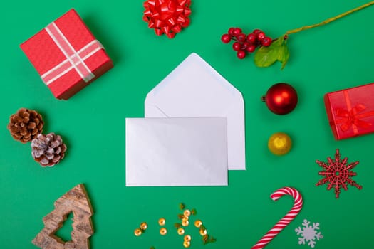 Composition of envelopes with christmas decorations and baubles on green background. christmas, tradition and celebration concept.