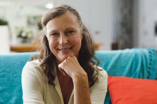 Portrait of happy senior caucasian woman in living room sitting on sofa, looking to camera. retirement lifestyle, spending time at home.