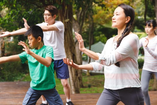 Asian parents, son and daughter exercising outdoors, practicing tai chi. family fitness time in garden.