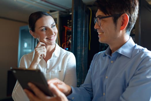 Diverse male and female engineers smiling while using digital tablet in computer server room. database server management and maintenance concept