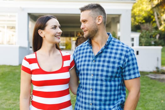 Smiling caucasian couple outside house looking at each other in garden. couple spending time at home.