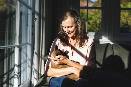 Happy senior caucasian woman in bedroom, holding her pet cat. retirement lifestyle, spending time alone at home.