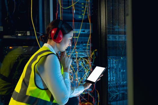 Thoughtful caucasian female engineer using digital tablet in computer server room. database server management and maintenance concept